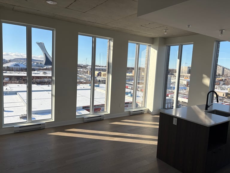 Empty modern office or apartment interior with floor-to-ceiling windows overlooking a city skyline, concrete flooring, and a black counter on the right.
